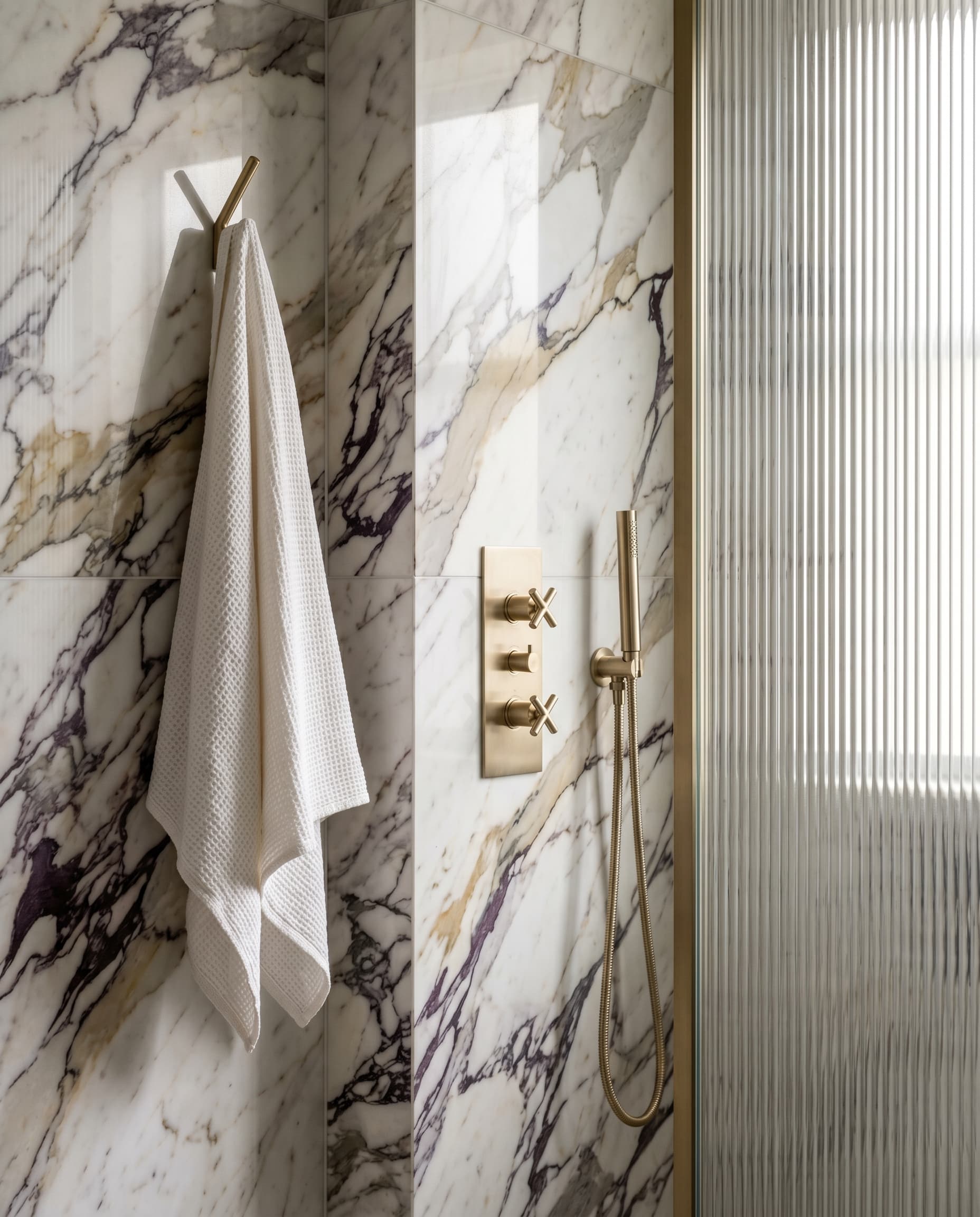 Finished corner of a bathroom: Calacatta Viola marble meeting champagne brass with a folded white linen towel